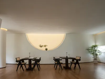 Minimalist restaurant interior with hardwood flooring, black tables, and white walls with a circular light fixture.