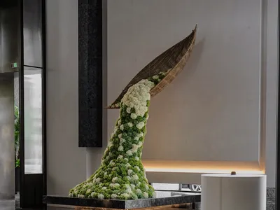 A modern hotel lobby featuring a mixed-materials sculpture on a marble platform.
