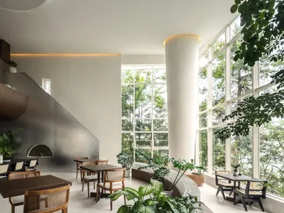 A stylish modern restaurant interior with concrete walls, wooden tables, and large windows overlooking greenery.