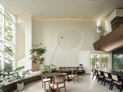 A modern restaurant interior with wooden furniture, white walls, and large windows.