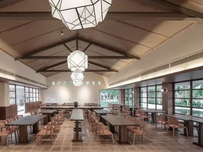 Modern restaurant interior with wooden tables and chairs, geometric light fixtures, and large windows.