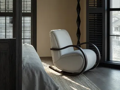 A serene bedroom interior featuring a white upholstered rocking chair, a floor lamp, and a bed with neutral-toned bedding and