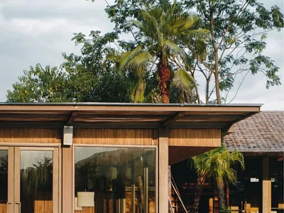 Industrial-style restaurant with wooden tables and chairs, surrounded by greenery and palm trees.
