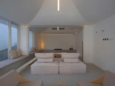 Minimalist living room with concrete walls, floor, and furniture. Light wooden coffee table with teapot and cups.