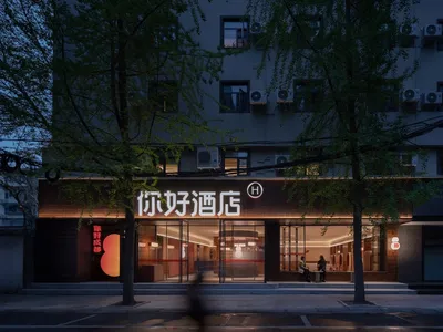The storefront of a hotel featuring glass walls, concrete elements, and illuminated lighting fixtures at dusk.