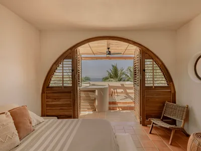 Bedroom with wooden doors and tile floor, featuring a bed with striped bedding and a wicker chair