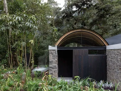 A modern minimalist spa hotel entrance featuring stone and wooden elements surrounded by lush greenery.