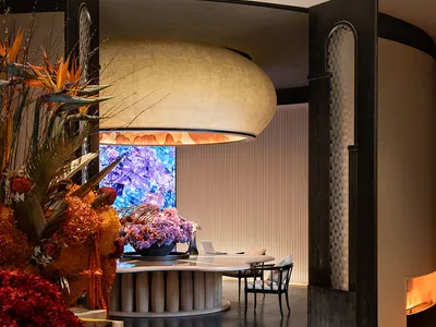 A modern restaurant interior featuring wood tables, fabric seating, and glass installations