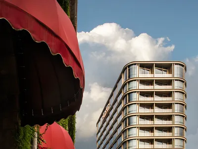 Outdoors shot of modern hotel with curved glass architecture, balconies, and lush greenery.