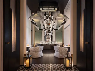 Modern restaurant interior with a glass chandelier, wooden tables, and fabric chairs