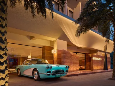 A classic blue and white car parked in front of a luxurious hotel entrance with concrete and marble finishes.