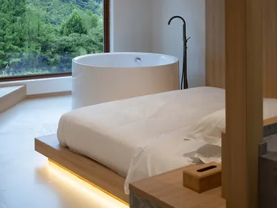 A minimalist bedroom featuring a freestanding bathtub overlooking a lush green landscape through a large window.