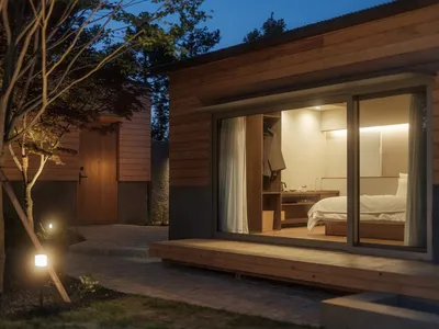A serene, minimalist bedroom featuring wooden furnishings and a window overlooking the surrounding trees.