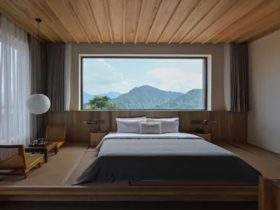 A minimalist bedroom featuring a wooden platform bed with a view of mountains through a large window.