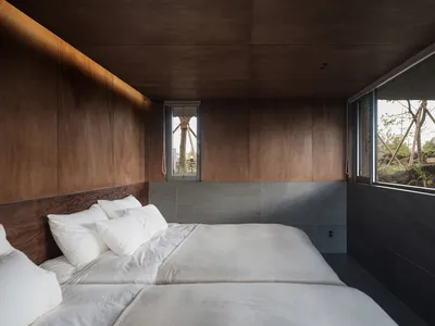 A minimalist bedroom featuring a bed with white bedding and wooden walls, viewed from the side.