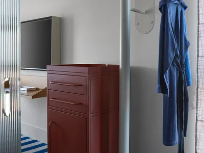 A minimalist bedroom featuring a red metal cabinet on wheels and a blue and white striped rug.