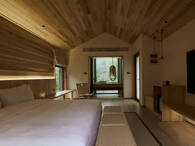 A minimalist bedroom featuring wooden furniture and a large window with a view of nature.