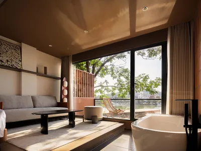 A minimalist hotel suite featuring concrete walls, wooden furniture, and floor-to-ceiling windows with a view of the outdoors