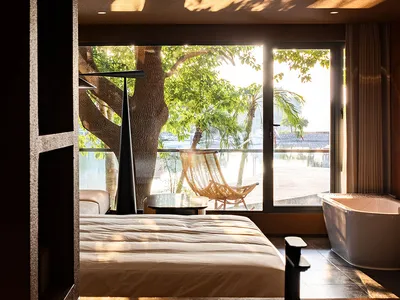 A modern bedroom with a balcony featuring wooden furniture, glass walls, and concrete elements.