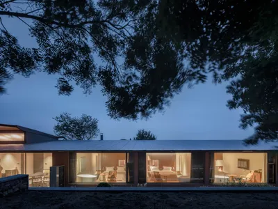 A modern bedroom featuring large glass windows and concrete surfaces, illuminated at dusk.