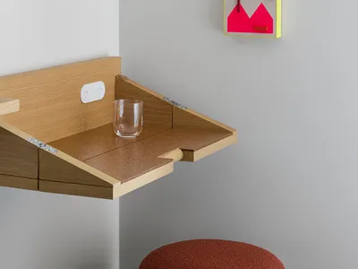 A minimalist home office space featuring a wooden desk with a glass surface, a glass tumbler, and a colorful abstract wall ar