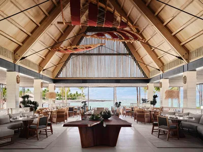 A spacious restaurant interior featuring wooden beams, open layout, and a view of the ocean.