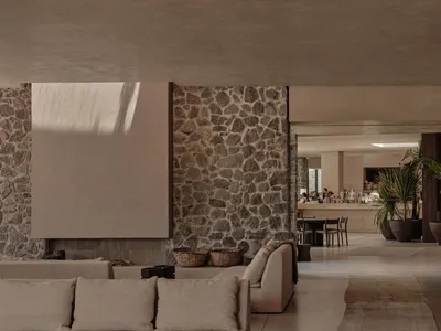 A minimalist lounge area with concrete furniture and flooring, featuring a stone wall and natural light.