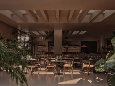 A modern restaurant dining room with wooden tables, glass pendant lights, and green plants.