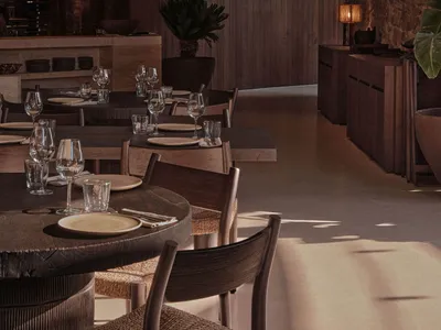 A modern restaurant interior with round wooden tables, chairs, and a mix of natural and industrial materials.