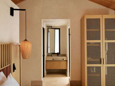 A minimalist bedroom featuring a bed with a wooden headboard, a hanging wicker pendant light, and a wooden closet with a grid