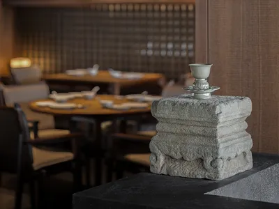 A stone pedestal with a small ceramic cup on top, set against the backdrop of an industrial-style restaurant interior with wo