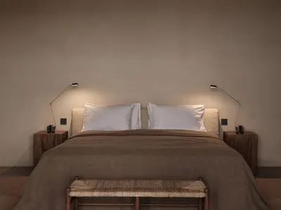 A minimalist bedroom featuring a bed with white pillows and a brown blanket, accompanied by two bedside lamps and a wooden be
