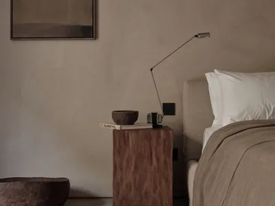 A minimalist bedroom featuring a wooden nightstand and bed, with a simple lamp and decorative bowls.
