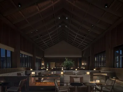 A spacious modern hotel lounge with high ceilings, wooden beams, stone tables, and metal chairs.
