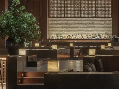 A modern restaurant bar with dark wood materials and a focus on the bar area with bottles and lighting.
