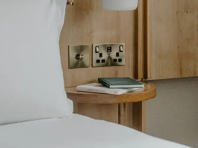 Minimalist bedroom featuring a wooden headboard and nightstand with books and a lamp.