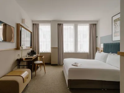 A modern hotel room with a king-sized bed, a work desk, and a large window.
