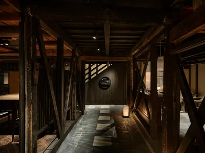 An industrial-style restaurant interior with a dark, wooden hallway leading to a seating area.
