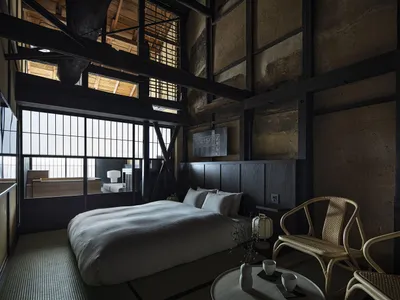 Minimalist bedroom featuring wood elements, with a large bed, two wicker chairs, and a low table in the foreground.