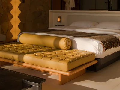 A minimalist bedroom featuring a wooden bed frame, a leather bench, and a stone wall.
