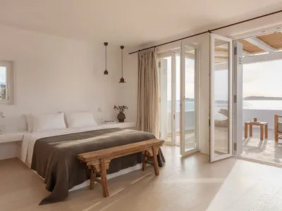 Minimalist bedroom featuring a wooden bed frame and wooden furniture, with a view of the sea through open glass doors.