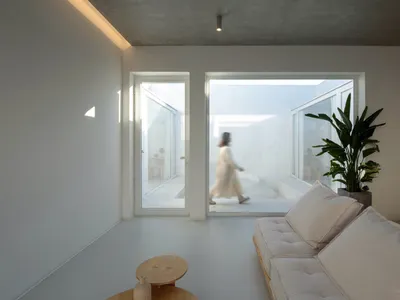 極簡客廳，混凝土牆面與地板，大型窗戶，以及米色沙發。