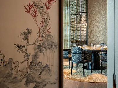 A minimalist restaurant interior with a round table and chairs, white walls, and a decorative fabric pattern.