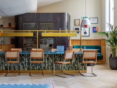 A modern restaurant bar with wooden and cane furniture, copper railings, and glass panels.