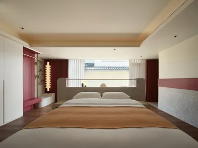 一間現代住宅臥室，床鋪採用水磨石與混凝土質感，搭配簡約設計與紅色點綴。