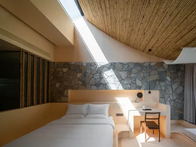 A serene, minimalist bedroom with concrete walls, a skylight, and a view of the mountains.