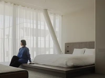 A serene minimalist bedroom with a white bed, grey carpet, and a wooden headboard.