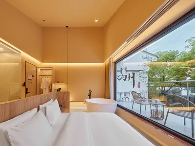 簡約臥室擺設白色家具，搭配大型窗戶可俯瞰花園景觀。