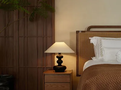 Minimalist bedroom with a wooden bed frame and nightstand, natural lighting, and greenery.