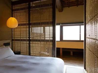 A minimalist bedroom with a bed, white sheets, and a wooden headboard.